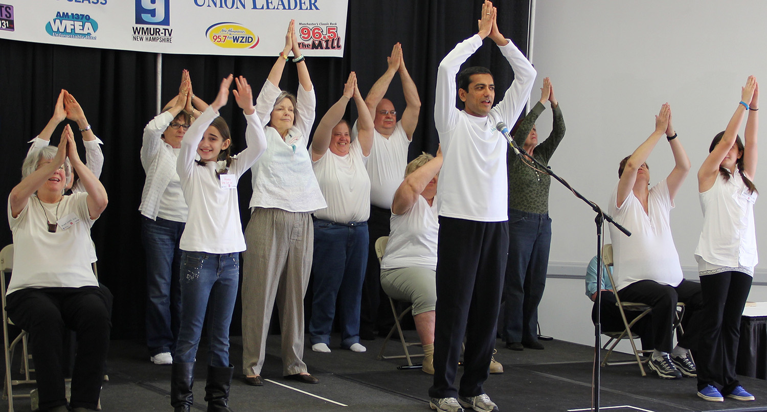 A group of elderly people performing a group exercise with arms raised.