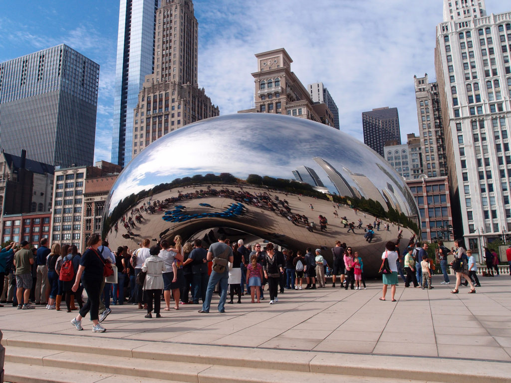 The Cloud Gate sculpture in Chicago filled with visitors on a sunny day.