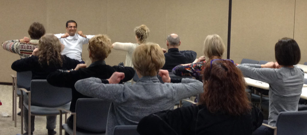 A group of people seated, raising their arms in unison during a session.