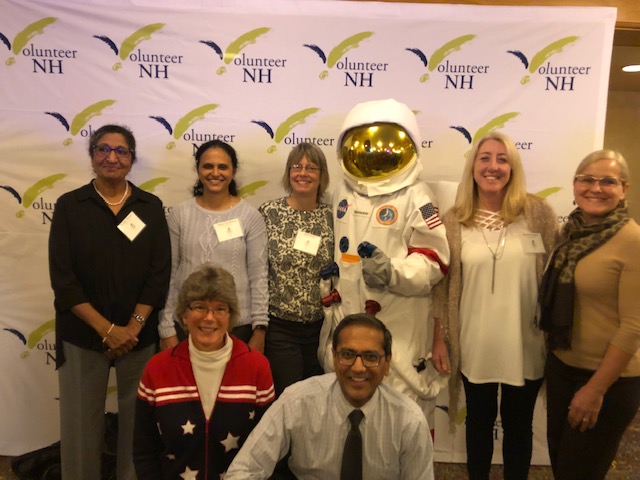 Group of professionals posing with a person in an astronaut suit at an event.