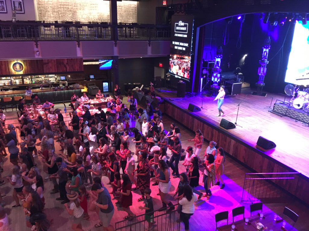 Crowd watching a live performance on stage in a large indoor venue.