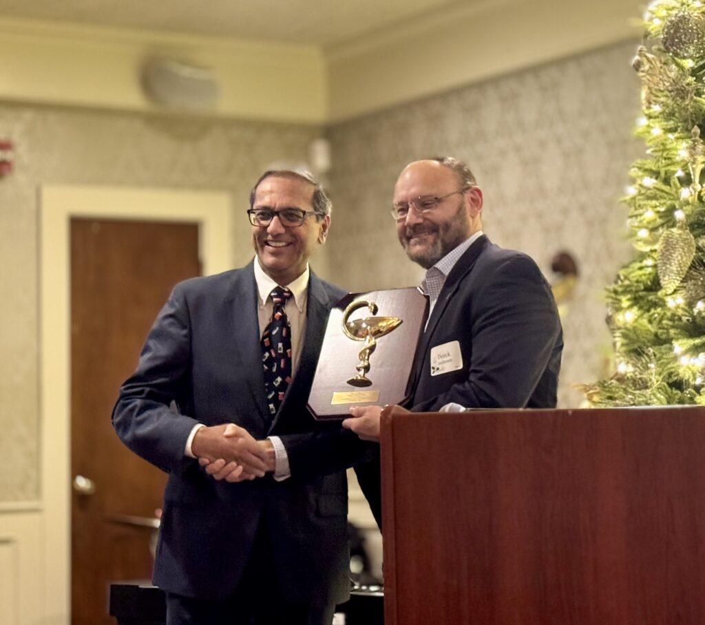 Two men shaking hands during an award presentation at a formal event.