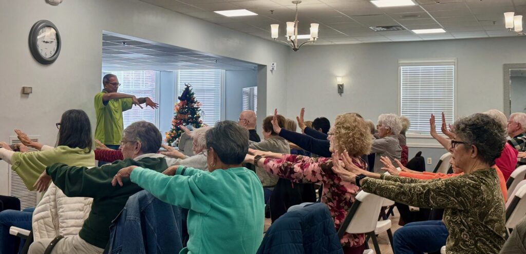 Group of elderly people exercising with arm stretches indoors.